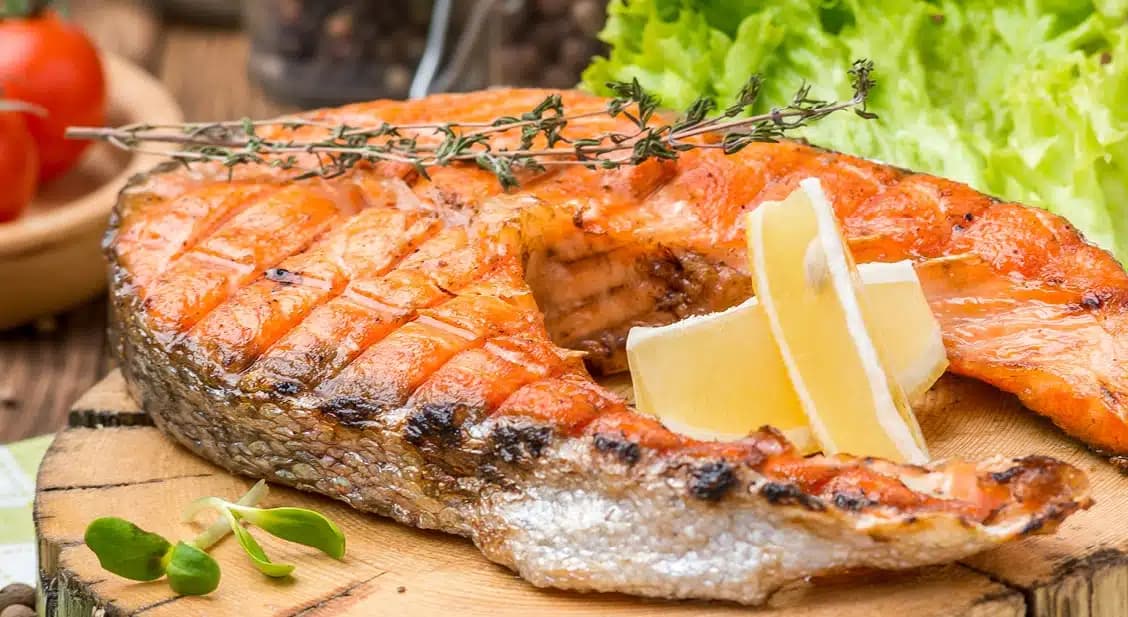 Grilled salmon steak with lemon and herbs on a wooden board